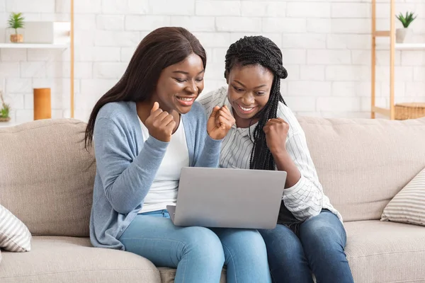 Dua gadis afro ceria merayakan keberhasilan dengan laptop di rumah — Stok Foto