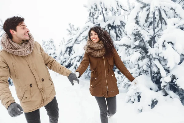 Улыбающаяся девушка и бойфренд, держащиеся за руки, идущие по зимнему лесу — стоковое фото