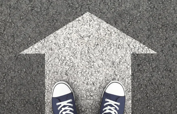 Chaussures bleues sur la route asphaltée avec flèche dessinée — Photo