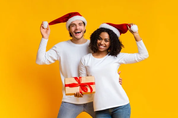 Glada multiracial par bär Santa hattar och poserar med julklapp — Stockfoto