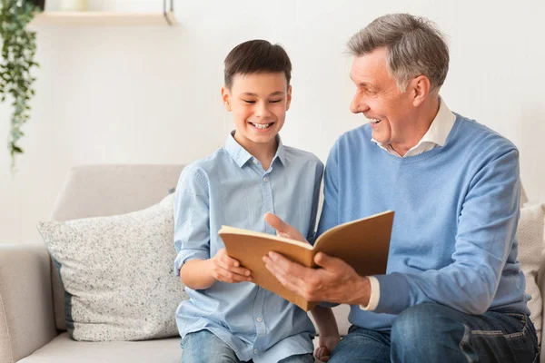 Senior man och pojke läsning bok sitter på soffan — Stockfoto