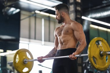 Genç kaslı vücut geliştirici halterle ağırlık kaldırıyor.