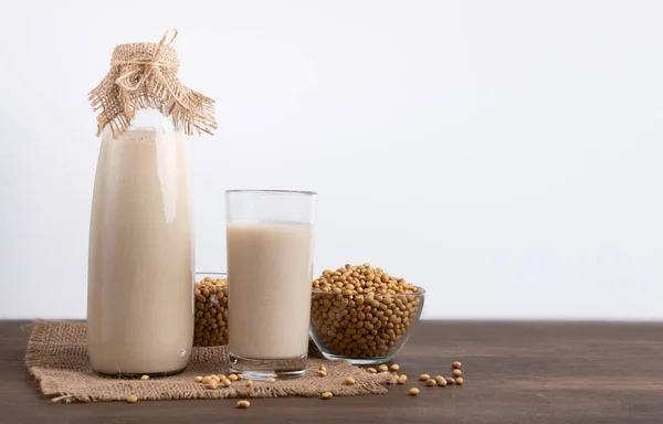 Соевое молоко и бобы на деревенском столе, белый фон — стоковое фото