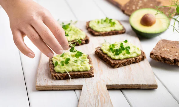 Girl decorating rye bread sandwiches with avocado spread — Stock Photo, Image