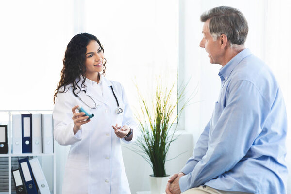 Врач показывает пожилому человеку синий ингалятор от астмы
