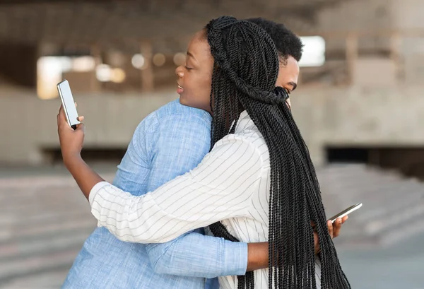 Preto cara e menina abraçando, mas olhando para smartphones sobre ombro — Fotografia de Stock