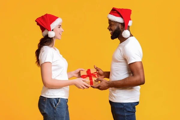 Loving multiracial couple in Santa hats exchanging Xmas gifts — Stock Photo, Image