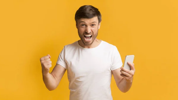 Homme émotionnel tenant le téléphone criant geste oui, fond jaune, panorama — Photo