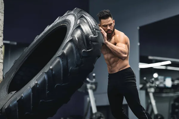 Shirtless muscular cara lançando enorme pneu no ginásio — Fotografia de Stock