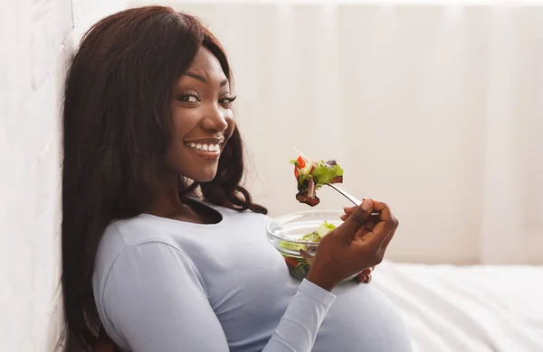 Leende gravid kvinna äter färsk sallad på sängen hemma — Stockfoto