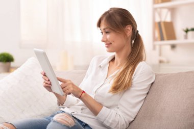 Tablet tableti kullanan gülümseyen bayan evde internet geziniyor.