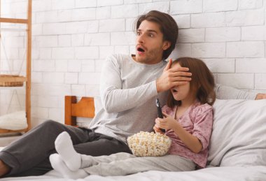 Baba ve anaokulu kızı evde film izliyorlar.