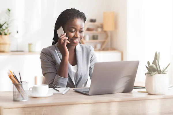 Siyah İş kadını cep telefonuyla konuşuyor ve iş yerinde dizüstü bilgisayar kullanıyor. — Stok fotoğraf