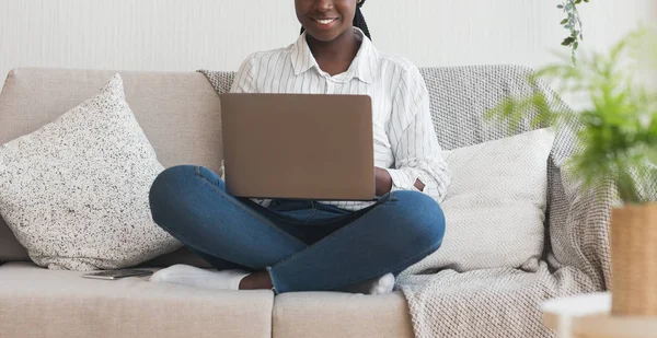 Méconnaissable fille noire assise sur le canapé avec ordinateur portable sur le tour — Photo