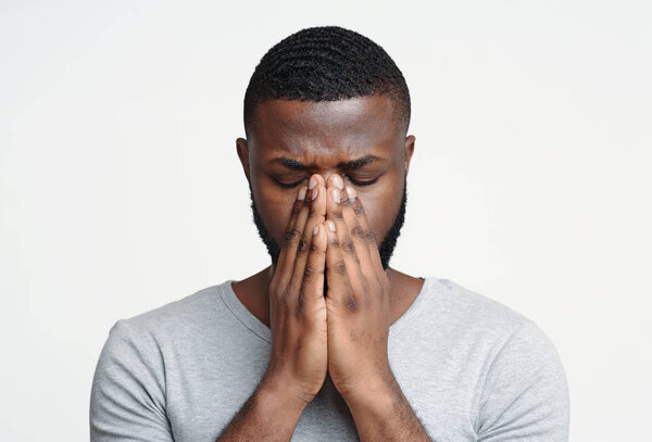 Грустный чёрный мужчина держит нос, потому что пазуха болит.
