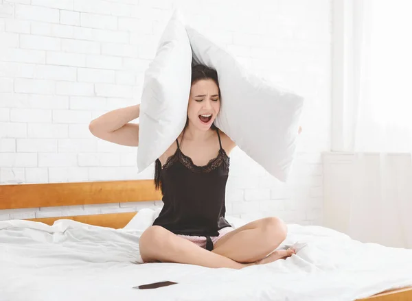 Mujer joven estresada gritando y cubriendo oídos con almohadas — Foto de Stock