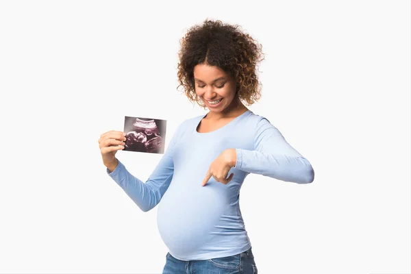 Felice signora incinta mostrando ecografie e indicando pancia — Foto Stock