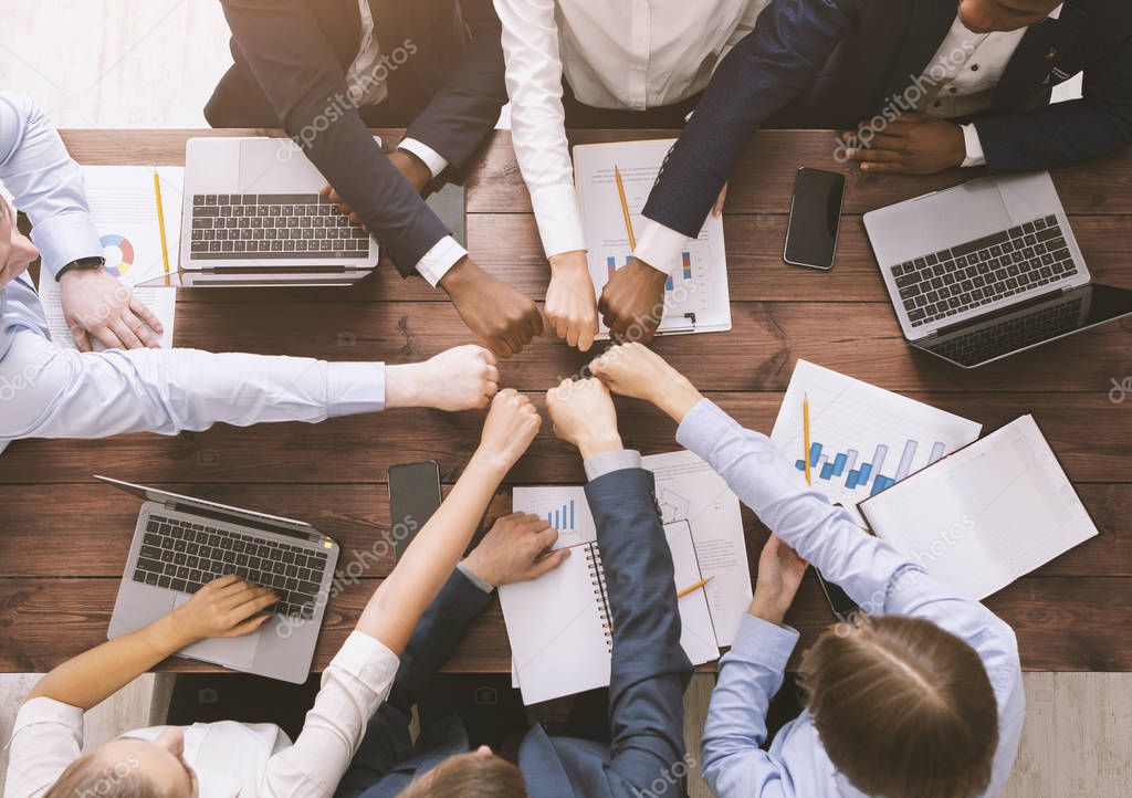 Fist bump of corporate team at meeting in office, top view