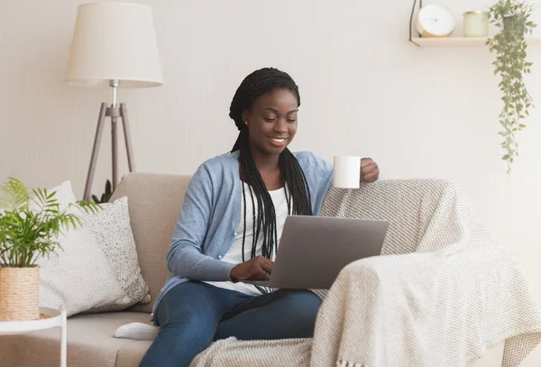 Μαύρο κορίτσι βλέποντας ταινία στο Laptop και πίνοντας καφέ στον καναπέ — Φωτογραφία Αρχείου