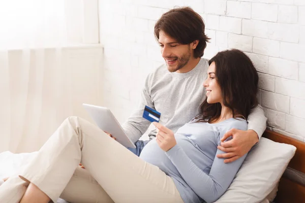 Pregnant couple using digital tablet and credit card for online shopping — ストック写真