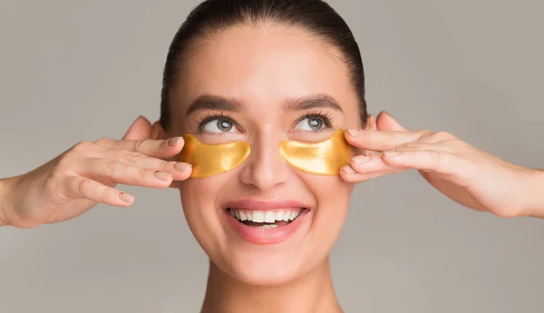 Pretty girl applying golden collagen patches under her eyes — Stock Photo, Image