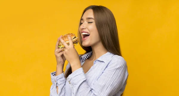 Mulher nova com fome comer hambúrguer de pé no estúdio, panorama — Fotografia de Stock