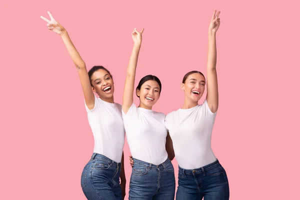 Tres chicas felices gestos V-Sign divertirse sobre fondo rosa —  Fotos de Stock