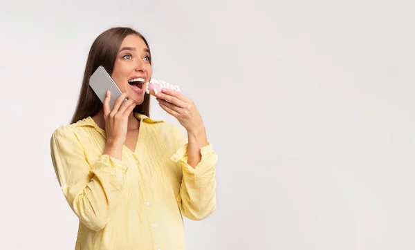 Chica embarazada hablando por teléfono comiendo donut sobre fondo gris — Foto de Stock