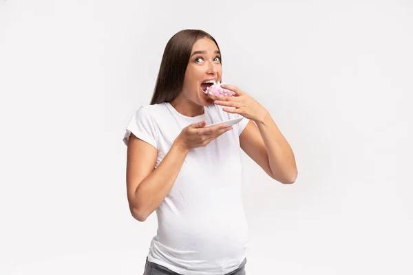 お腹が空いた妊婦が白い背景でドーナツをかむ、スタジオショット — ストック写真