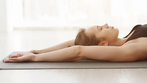 Relajada chica de yoga acostada en la estera, haciendo ejercicio respiratorio — Foto de Stock