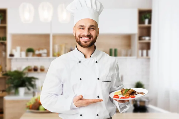 Happy Chef segurando placa com frango assado em pé na cozinha — Fotografia de Stock