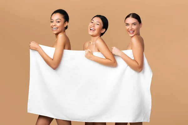 Three Girls Holding White Towel Smiling Posing Over Beige Background — Stock Photo, Image