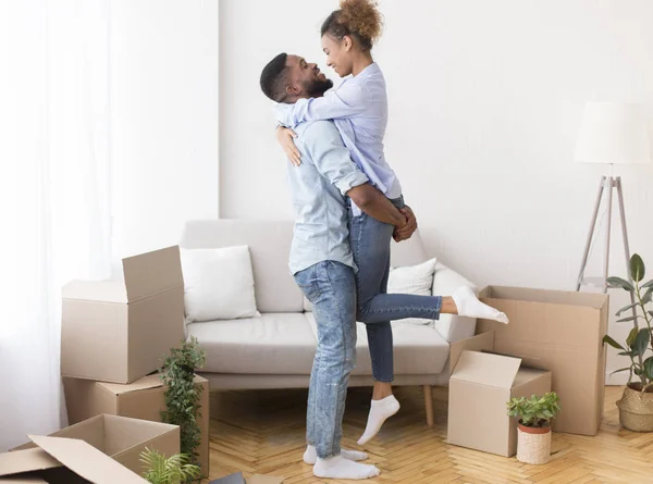 Парень поднимает подружку среди движущихся коробок в новом доме — стоковое фото