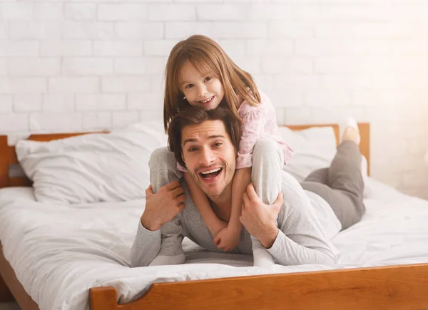 Dziewczyna siedzi na plecach ojca, przytula go i uśmiecha — Zdjęcie stockowe