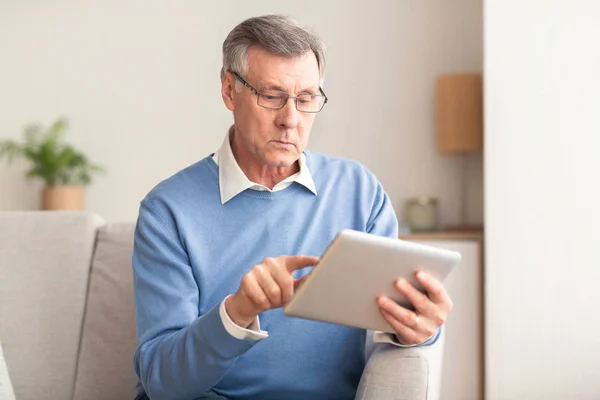 Ηλικιωμένος άνθρωπος χρησιμοποιώντας Tablet περιήγησης στο Internet κάθεται στον καναπέ — Φωτογραφία Αρχείου