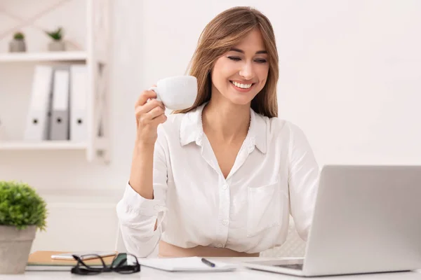 Feliz mujer de negocios en el ordenador portátil teniendo café sentado en la oficina —  Fotos de Stock