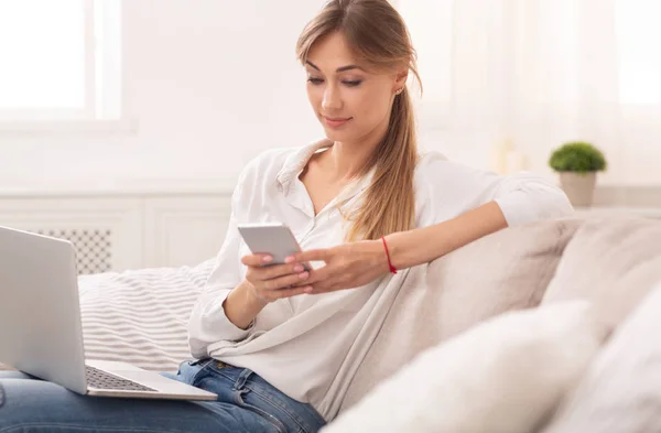 Frau schreibt SMS am Telefon und arbeitet zu Hause am Laptop — Stockfoto