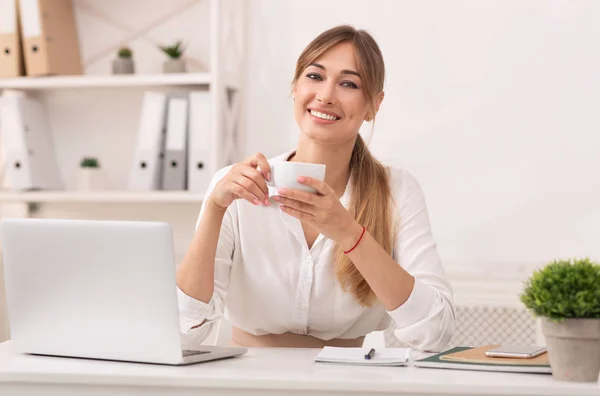 Modern ofiste elinde kahve tutan iş kadını kameraya gülümsüyor. — Stok fotoğraf