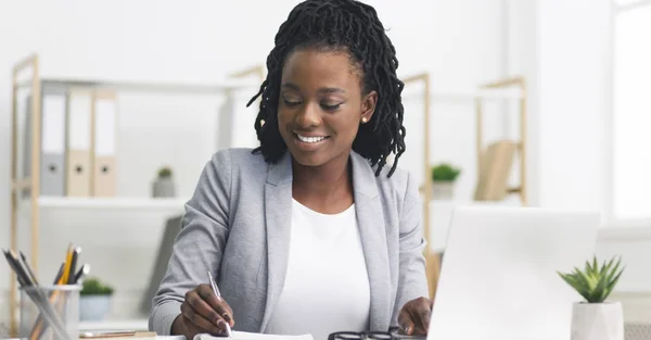 Preto millennial empresária tomando notas e trabalhando no laptop no escritório — Fotografia de Stock