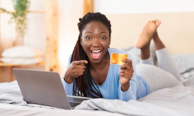 Yatakta kredi kartı alışverişinde parmaklarını gösteren heyecanlı kız.