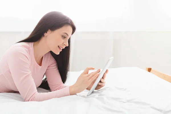 Chica alegre navegando en la tableta digital, descansando en la cama —  Fotos de Stock