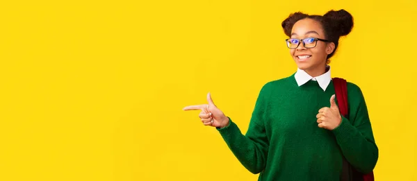 Black schoolgirl pointing at free space on yellow background — Stock Photo, Image