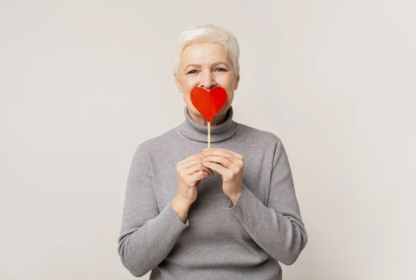 Senhora seniores românticos cobrindo boca com coração de papel — Fotografia de Stock