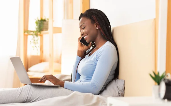 Afro-americano freelancer parlando su cellulare utilizzando computer portatile in camera da letto — Foto Stock