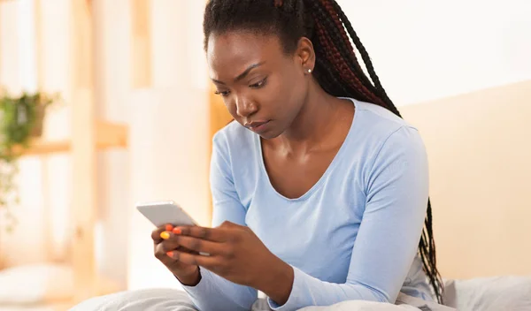 Chica seria usando el teléfono celular Mensajes de texto sentado en la cama en casa —  Fotos de Stock