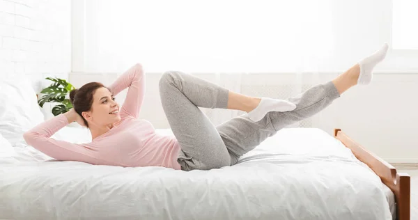 Sportovní dáma dělá fitnes, leží doma na posteli — Stock fotografie