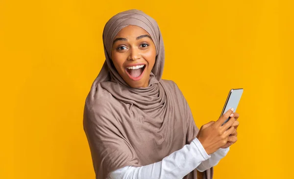 Retrato de niña afro musulmana excitada en hijab sosteniendo teléfono inteligente —  Fotos de Stock