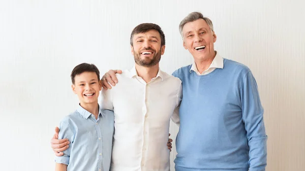 Man, Son and Elderly Father Embracing Standing Over White Wall — стоковое фото