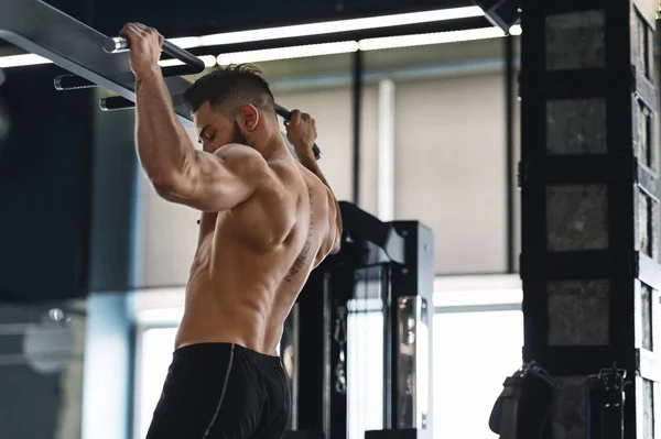 Atleta muscular tirando hacia arriba en la barra horizontal en el gimnasio —  Fotos de Stock