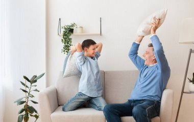 Mutlu büyükbaba ve torun Yastıklarla savaşıyor Koltukta oturuyor